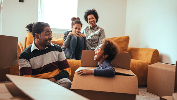 young family moving into new home playing with boxes and sitting on yellow sofa smiling and laughing
