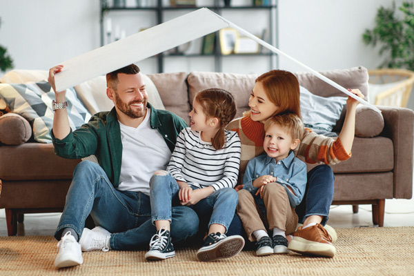 smiling happy young family in living room of home under white cardboard roof